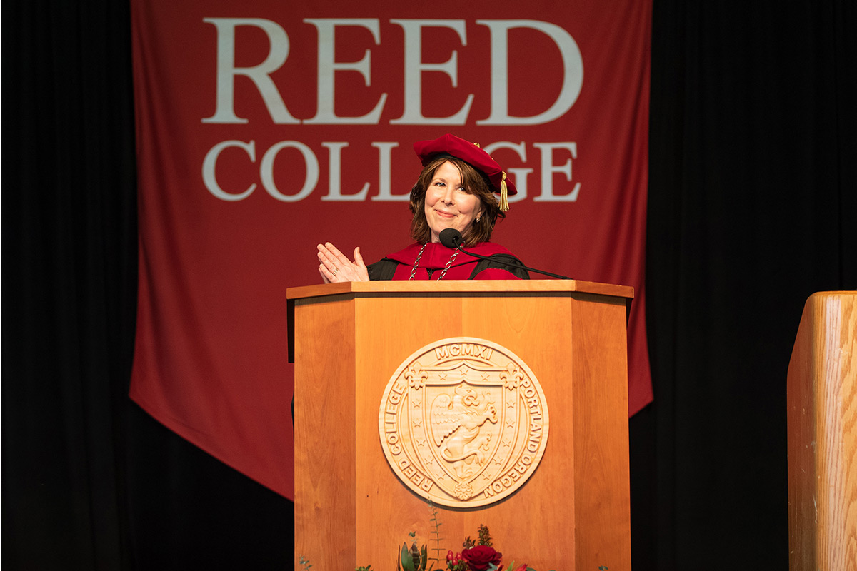 President Audrey Bilger applauds at a podium at Reed's 111th Commencement ceremony. 