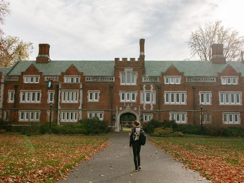 A student walks away from the camera toward Reed's residence hall Old Dorm Block.