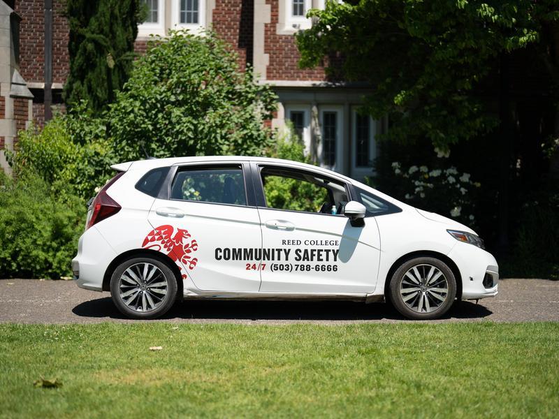 A white car with a Reed Community Safety decal on the door is parked in front of Eliot Hall.