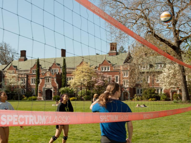 A ball sails over a volleyball net as two students reach for it.